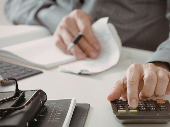 Coeficientes plusvalía municipal calculados por persona con una calculadora y documentos en una mesa.